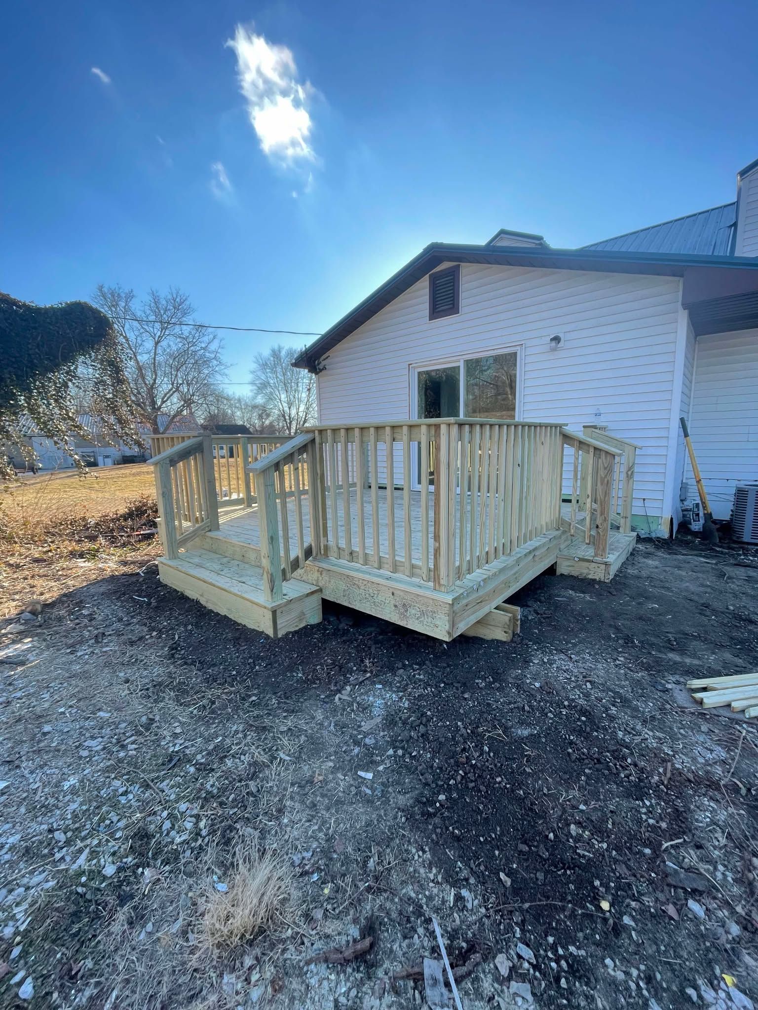 White house with a wooden wheelchair ramp and gravel yard under a clear blue sky