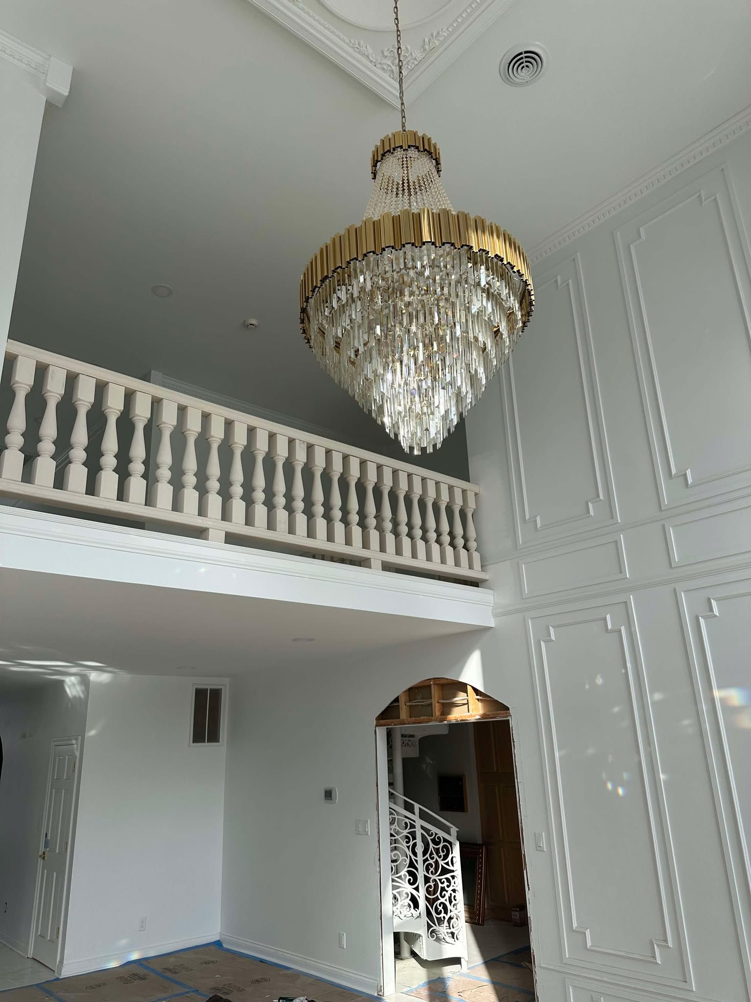 Elegant foyer with a large crystal chandelier, white paneled walls, and an upper balcony railing