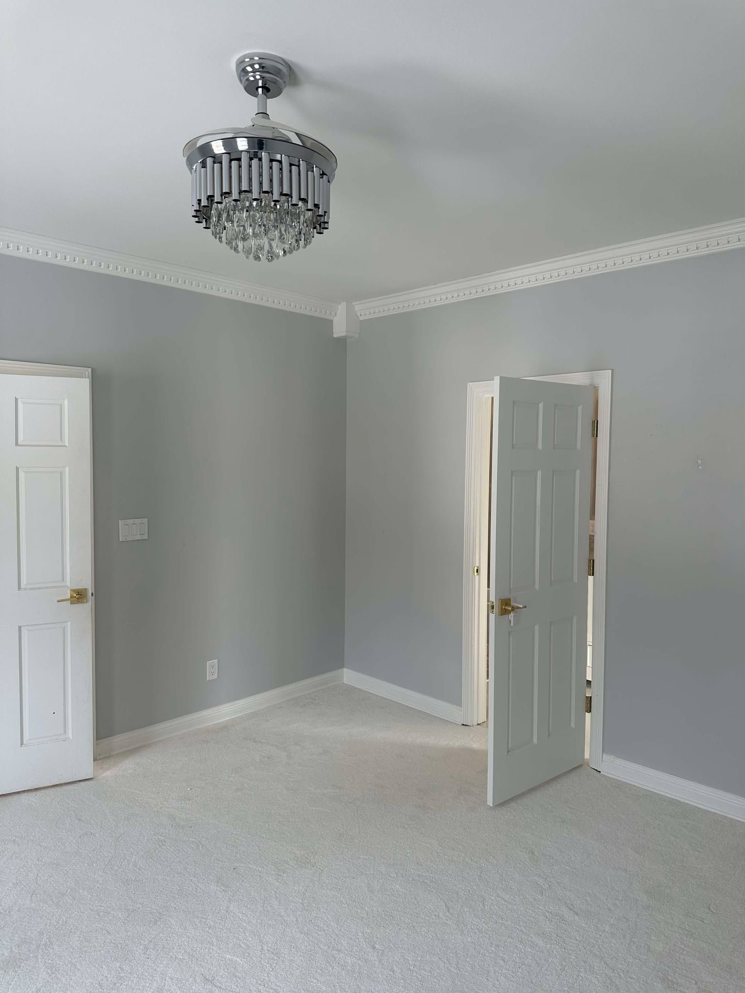 Empty gray bedroom with white trim, speckled carpet, chandelier, and open door.