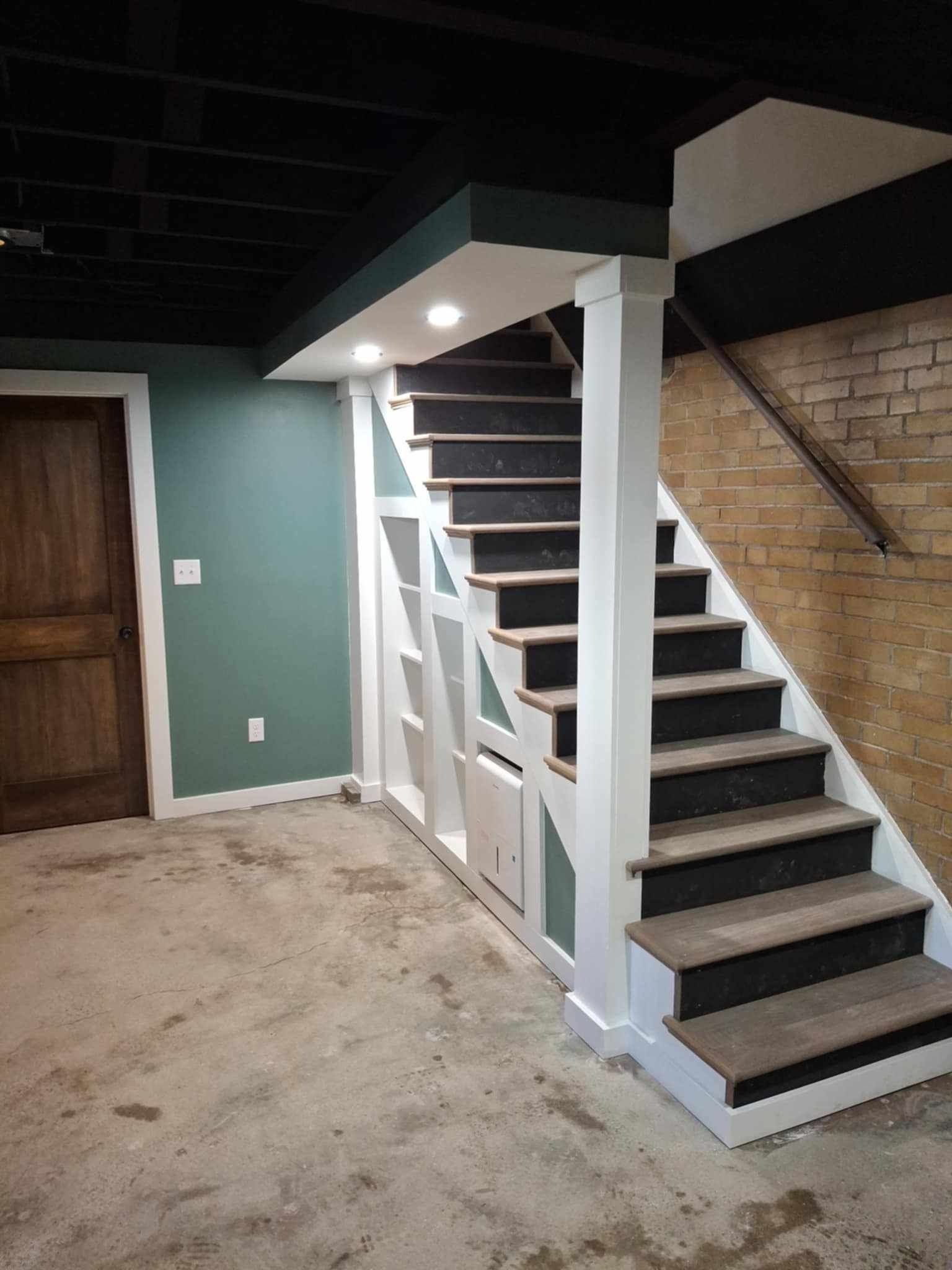 Basement staircase with dark steps and white railings beside a green wall and wooden door.