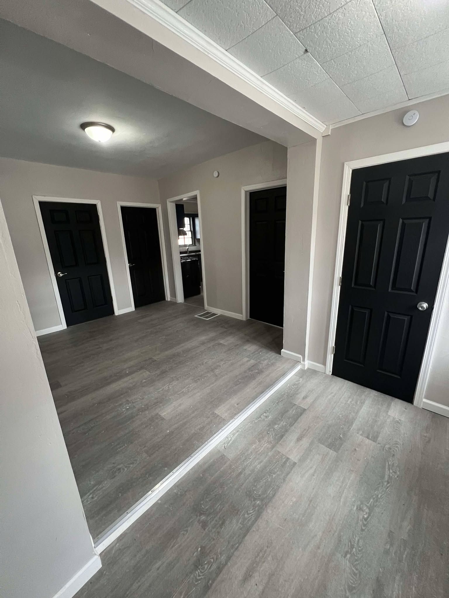 Empty hallway with gray wood floors, beige walls, black doors, and a ceiling light