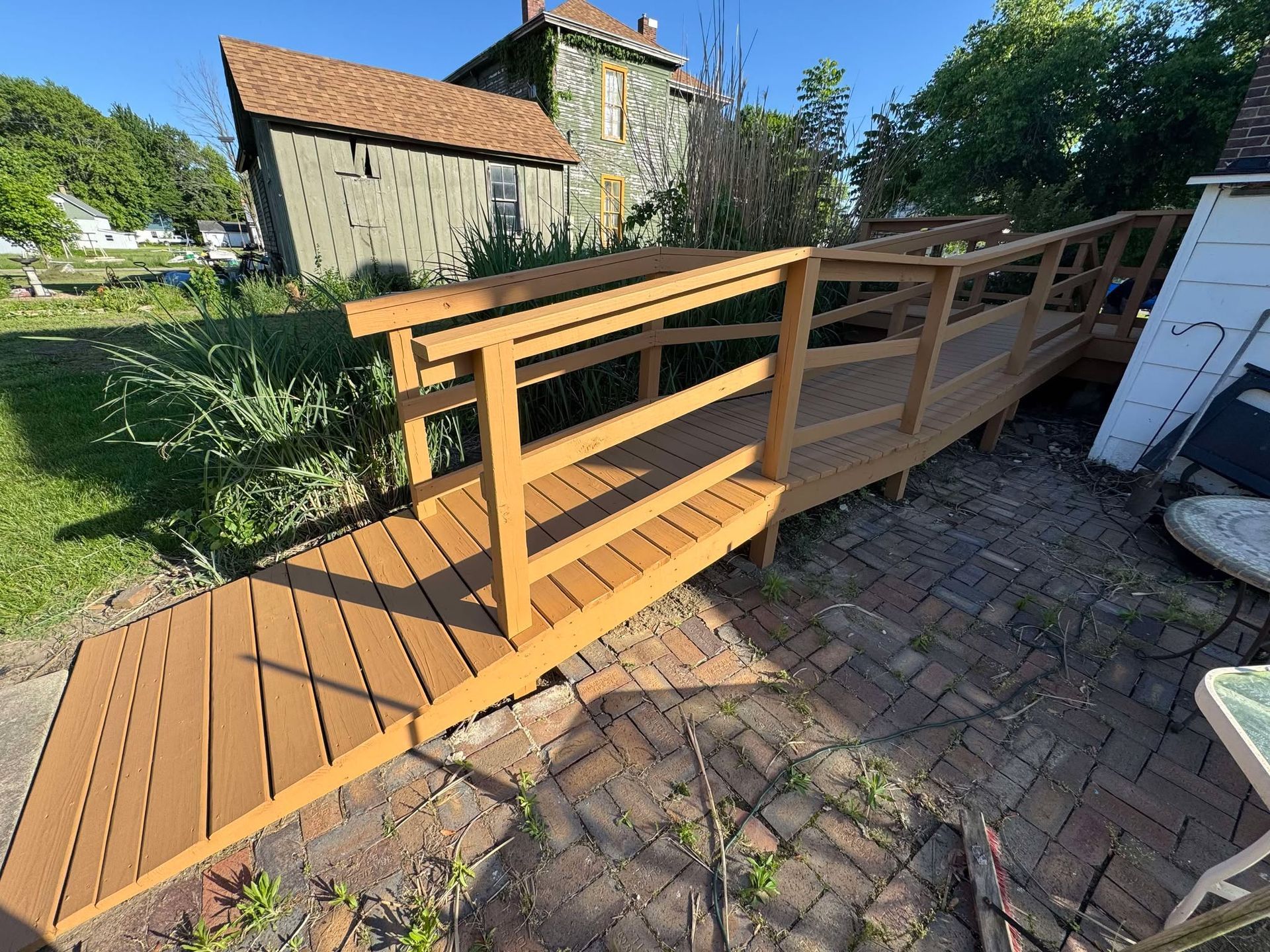 Wooden accessibility ramp with handrails leading to a house entrance in a sunny yard