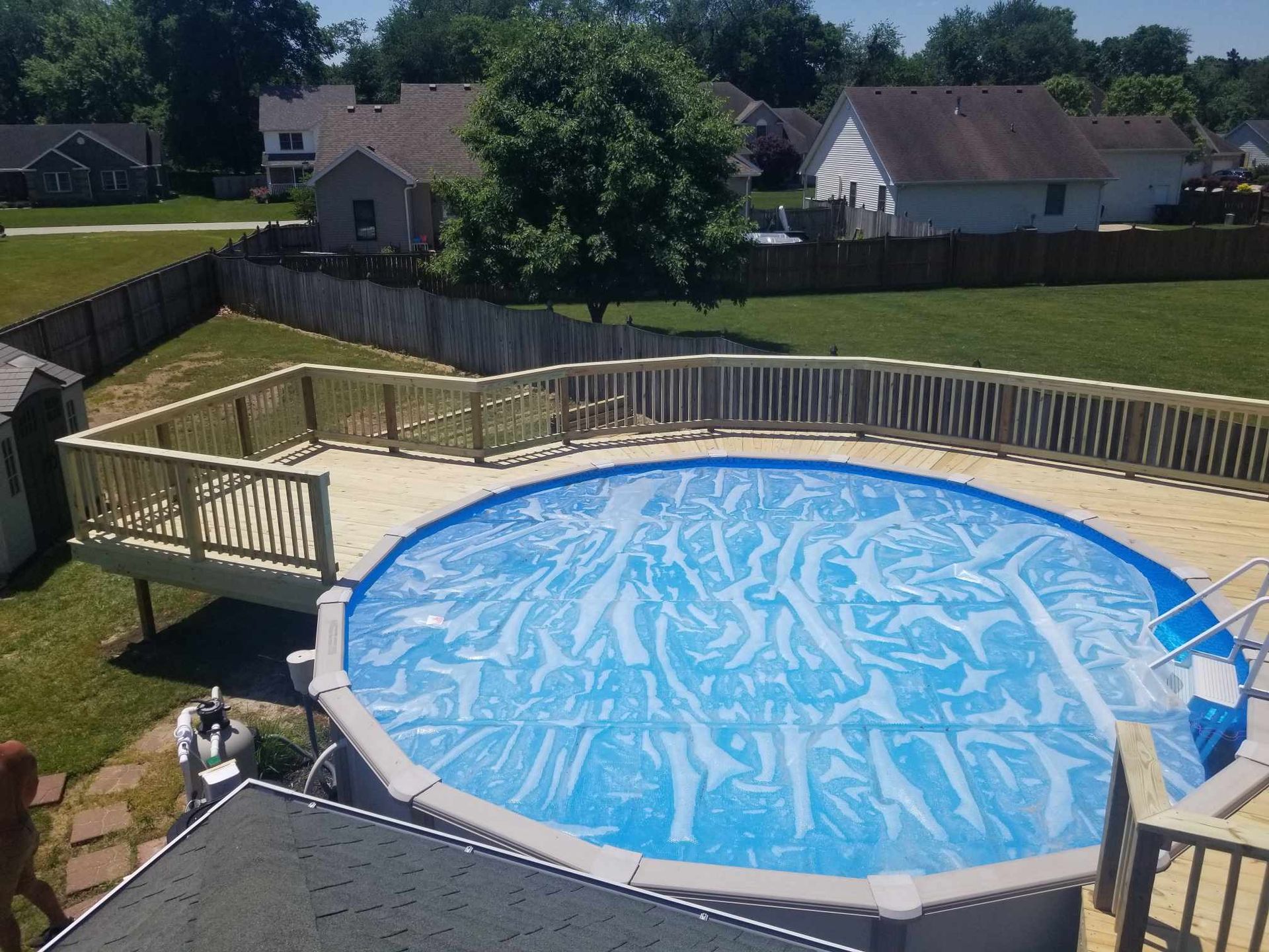 Empty above-ground pool with blue liner in a backyard, surrounded by a wooden deck and fence.