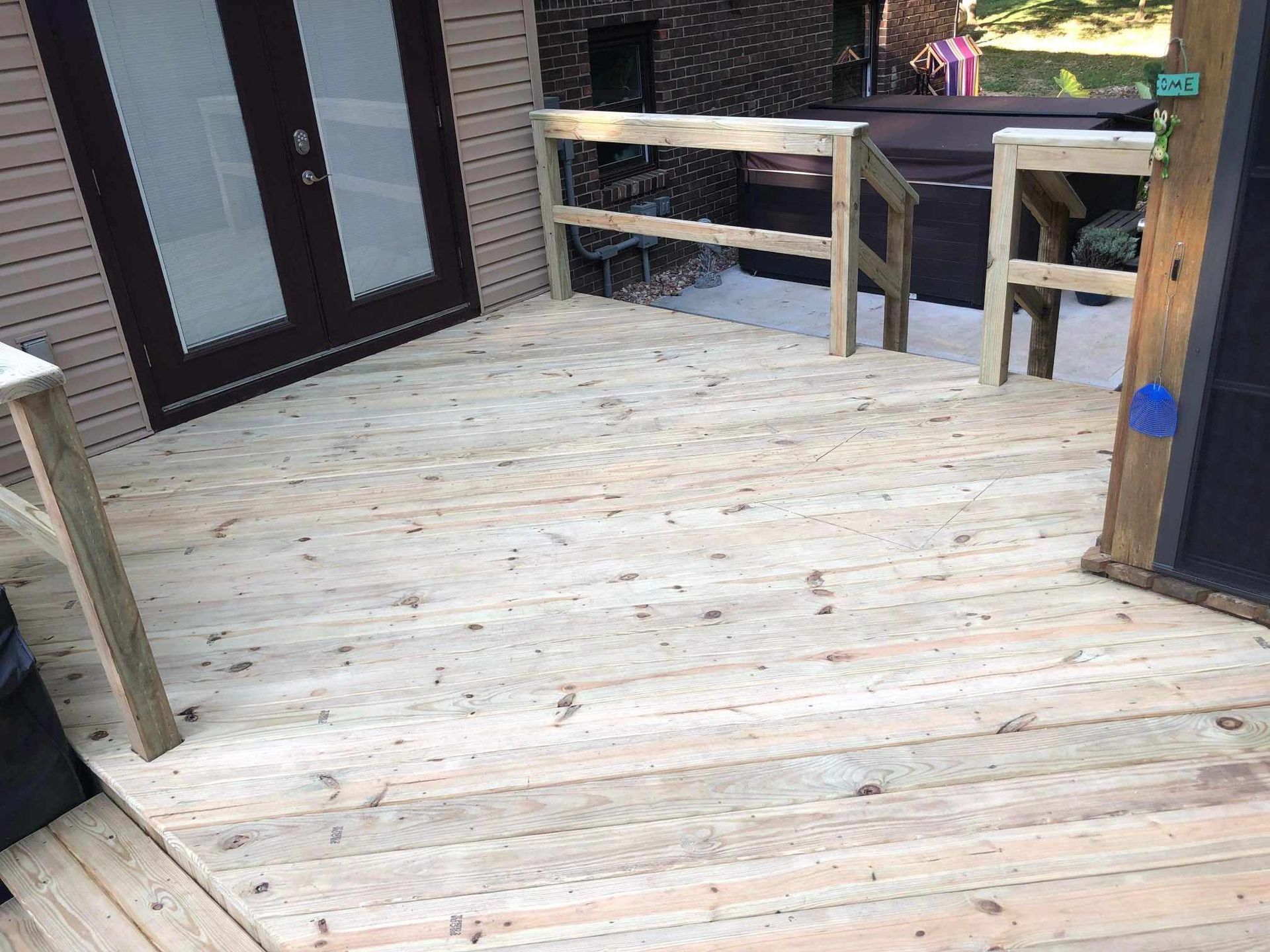 Wooden deck with railing beside a brick house and a glass door