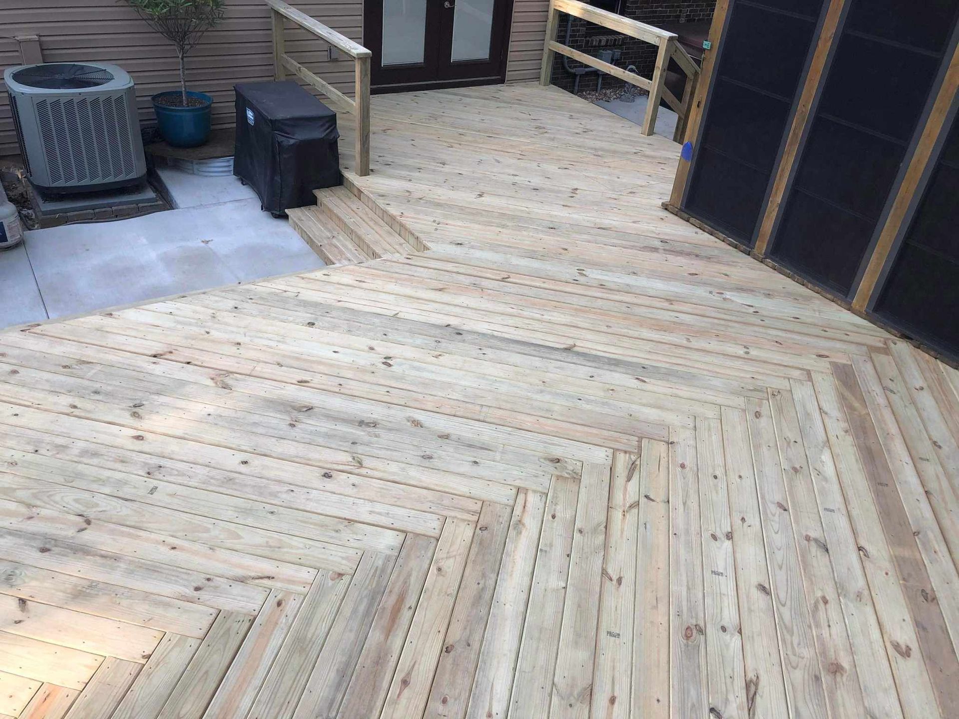 Wooden herringbone deck with planters and trash bins beside a building entrance