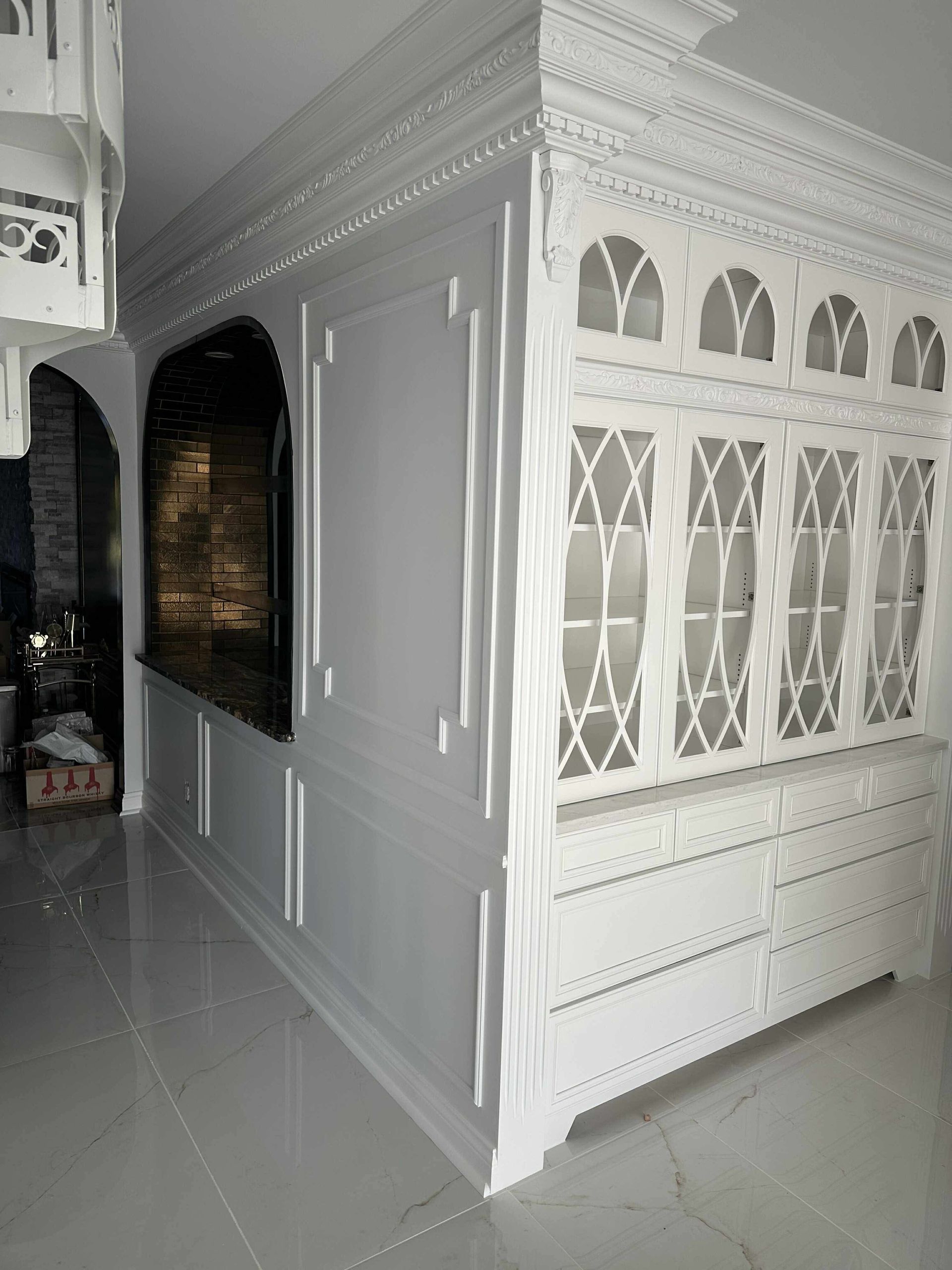 White ornate cabinet with glass doors and lattice detail in a tiled hallway