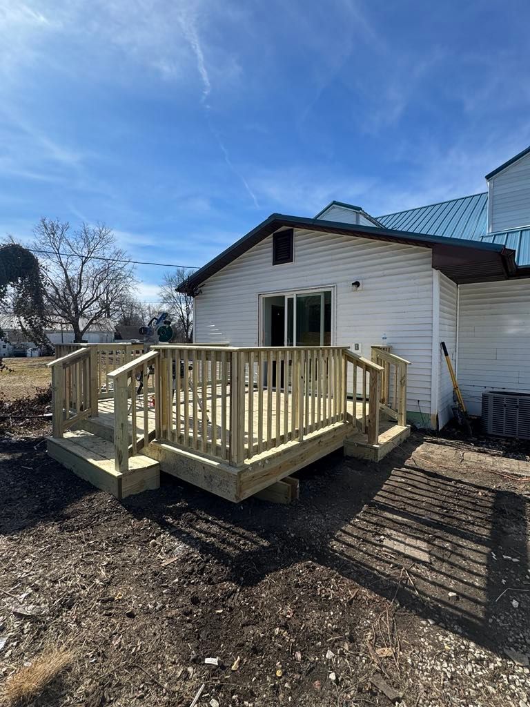 Small wooden accessibility ramp and deck attached to a white house under a blue sky.