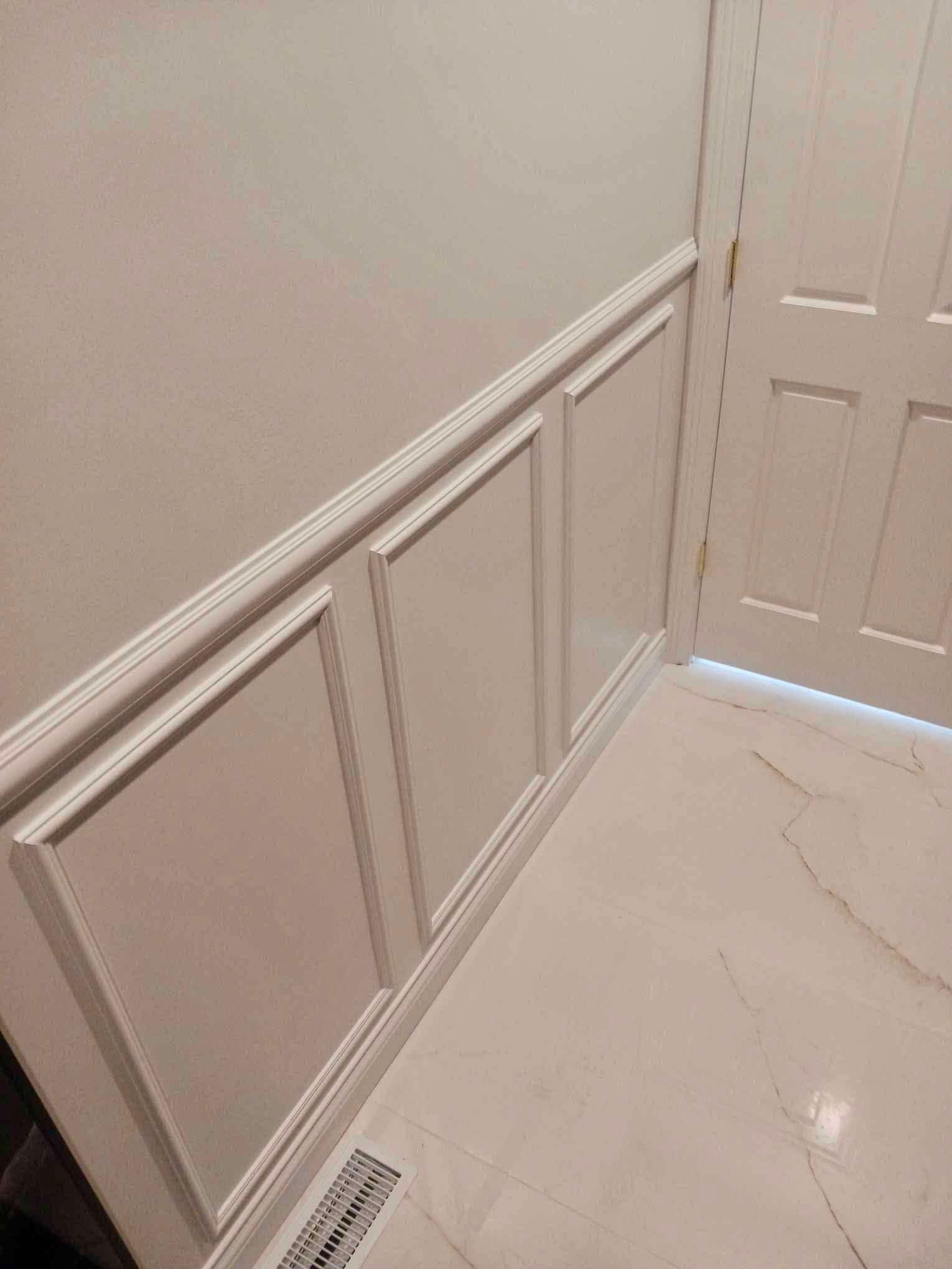 White hallway with wainscoting, a closed door, and a floor vent on a glossy floor.