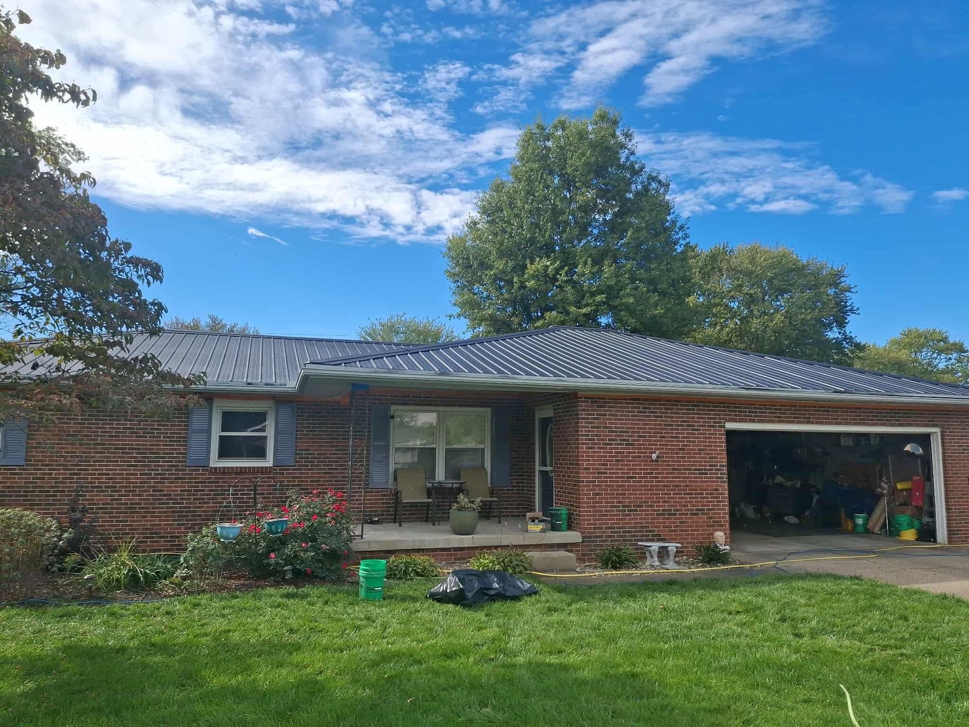 Brick house with a front lawn, covered porch, and open garage under a partly cloudy blue sky
