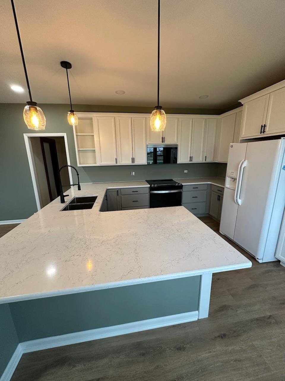 Modern kitchen with white cabinets, large island, pendant lights, and stainless steel appliances.