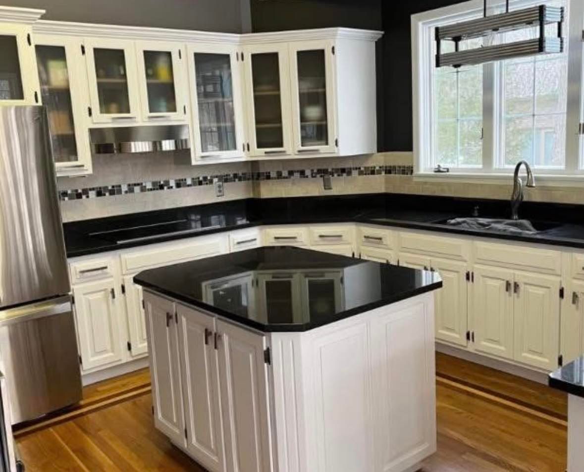 Bright kitchen with white cabinets, black countertops, stainless fridge, and a black island.