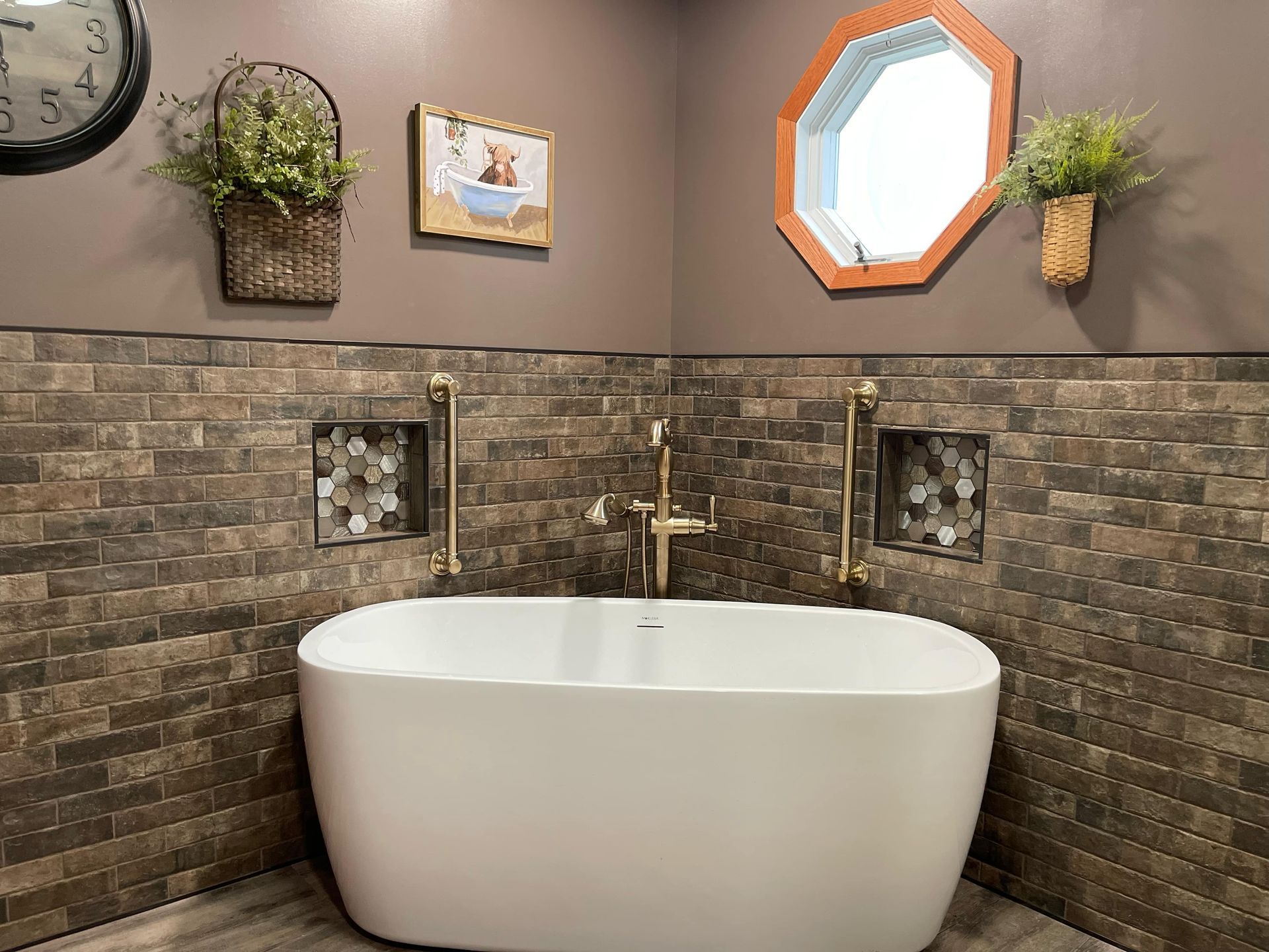 Modern bathroom with a freestanding white tub, stone accent wall, and gold fixtures