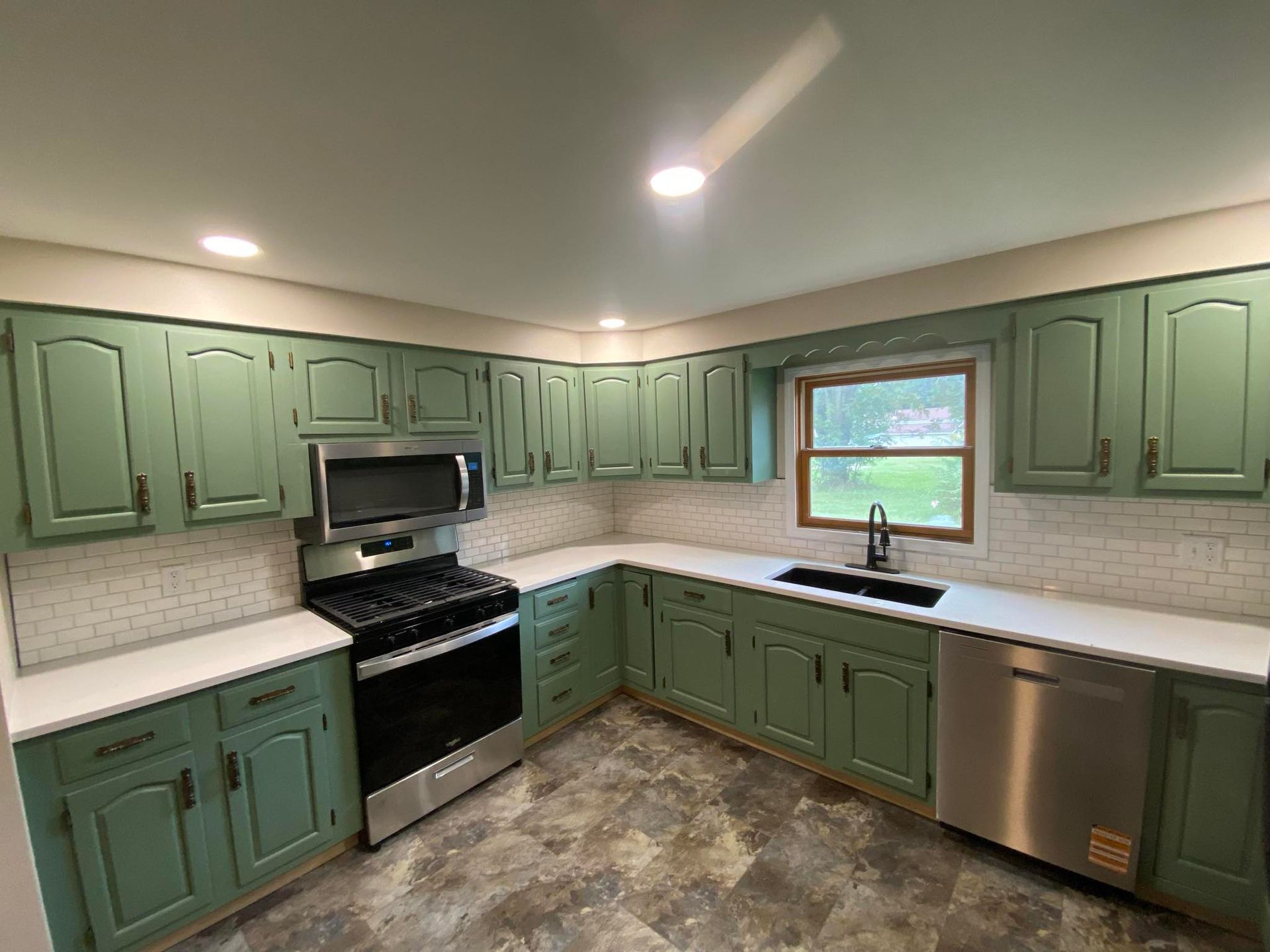 Green U-shaped kitchen with white counters, stainless steel appliances, and a window over the sink