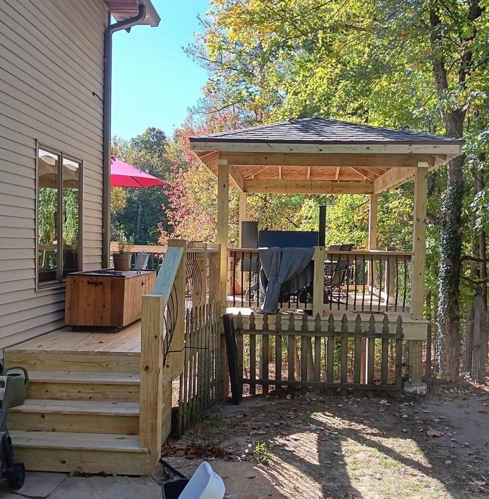 Backyard deck and gazebo beside a house, with wooden steps, railing, and trees in fall colors