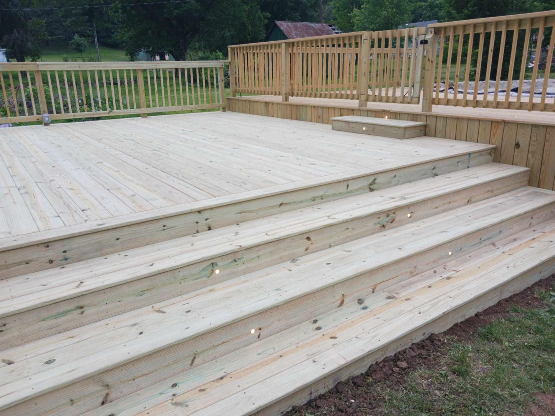 Wooden deck with three wide steps and railing overlooking a grassy yard and trees