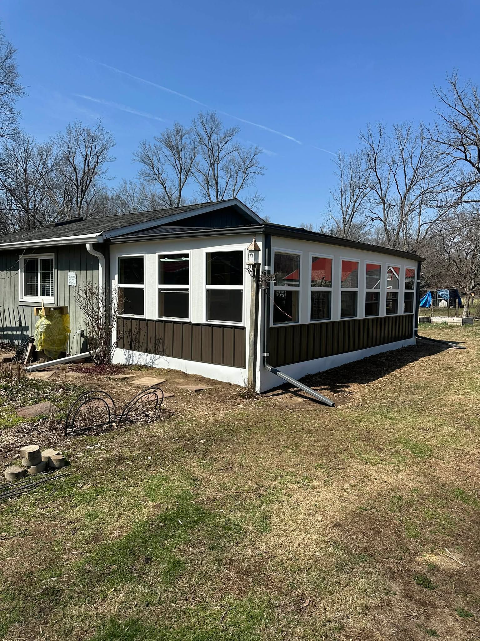 Small gray sunroom addition attached to a house in a grassy yard under a blue sky