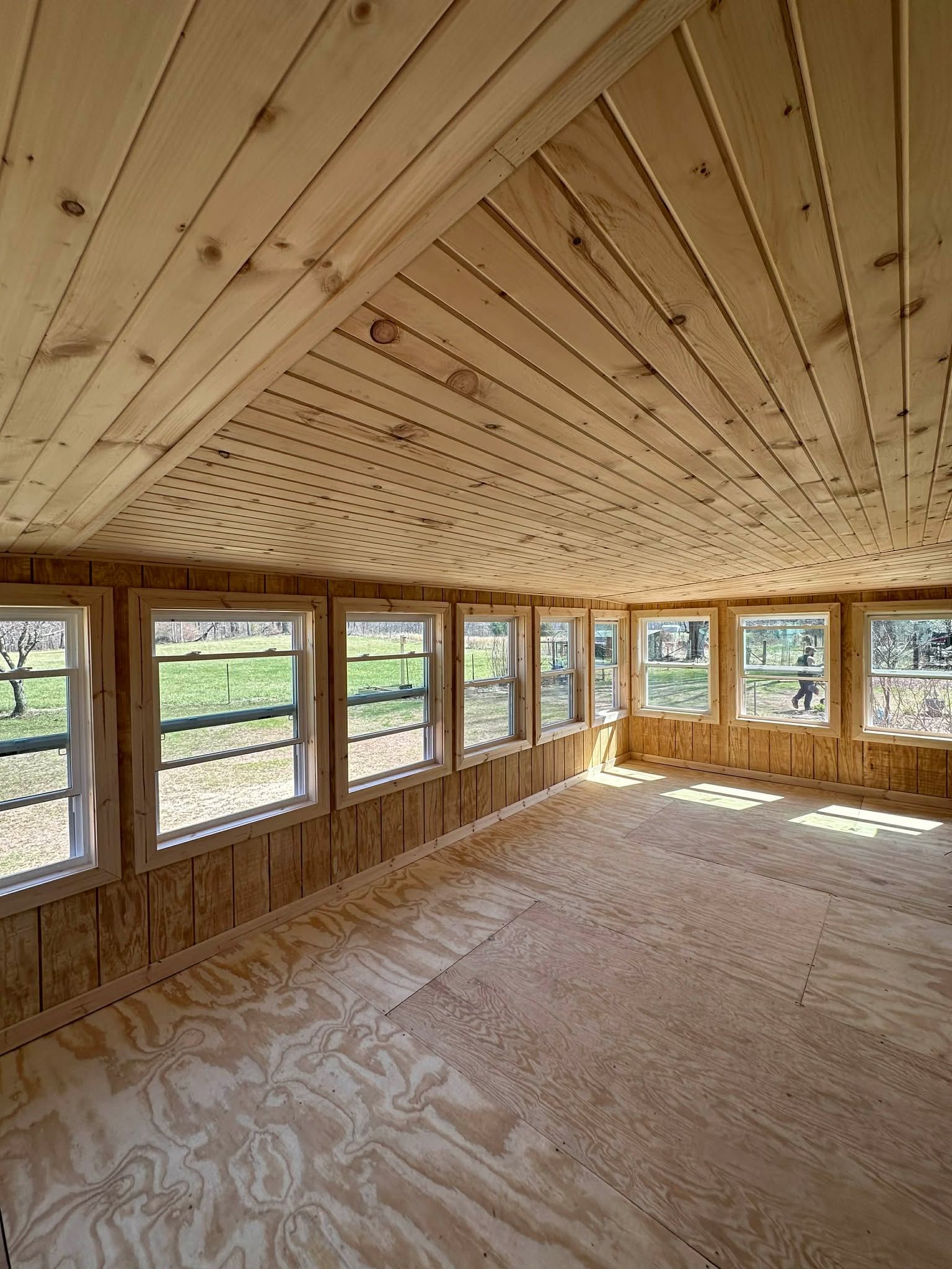 Unfinished wood-paneled room with rows of windows and a curved ceiling, filled with natural light.