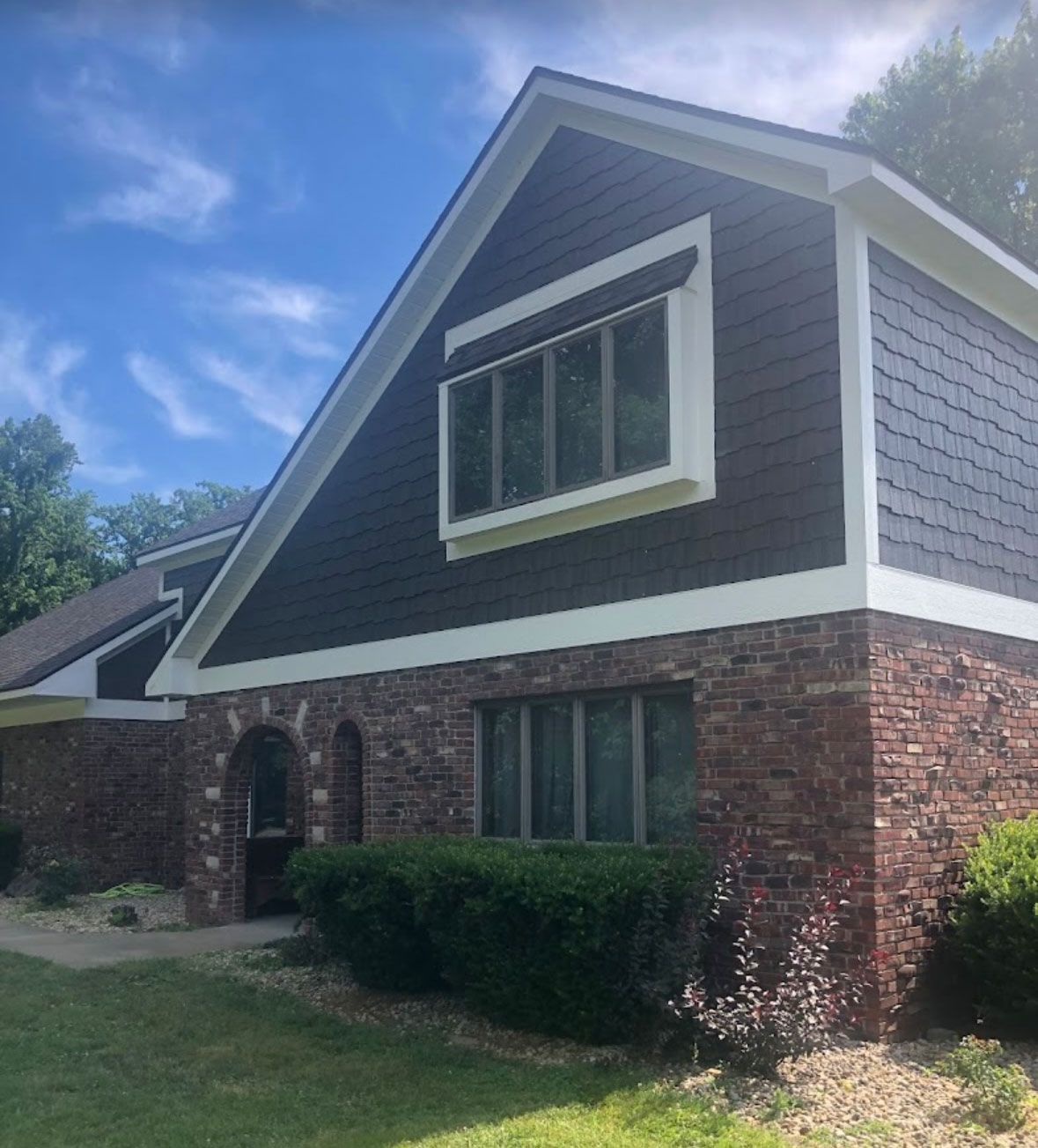 Two-story brick and dark-gray house with white trim and a steep gabled roof on a sunny day