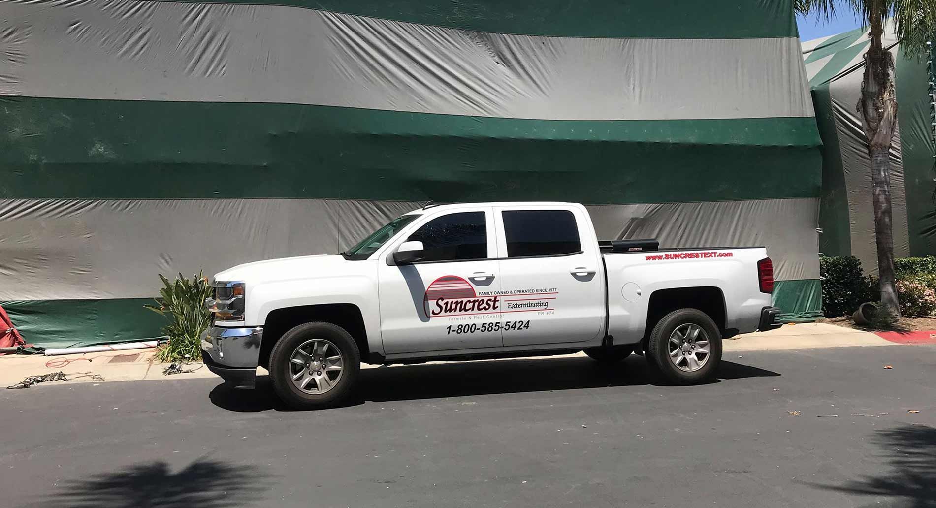 A white truck is parked on the side of the road in front of a green and white building.