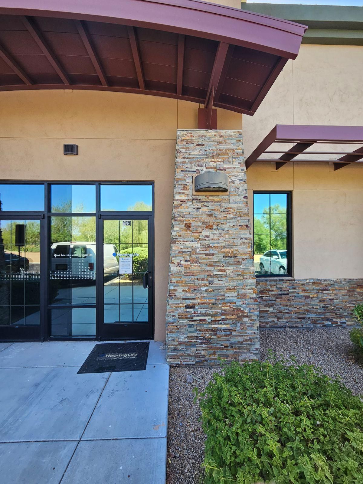 Entrance to a modern building with tan walls, a stone pillar, glass doors, and a brown metal awning.