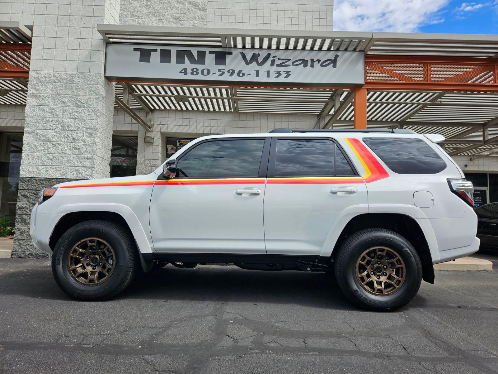 A white Toyota 4Runner with retro red, orange, and yellow side stripes parked outside Tint Wizard.