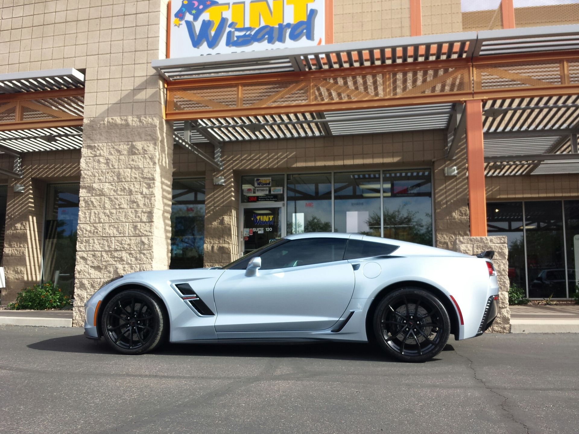 A silver Chevrolet Corvette parked in front of a storefront building titled 