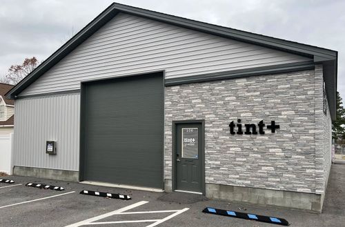 Gray commercial building with a large garage door and the sign “tintt” on the front