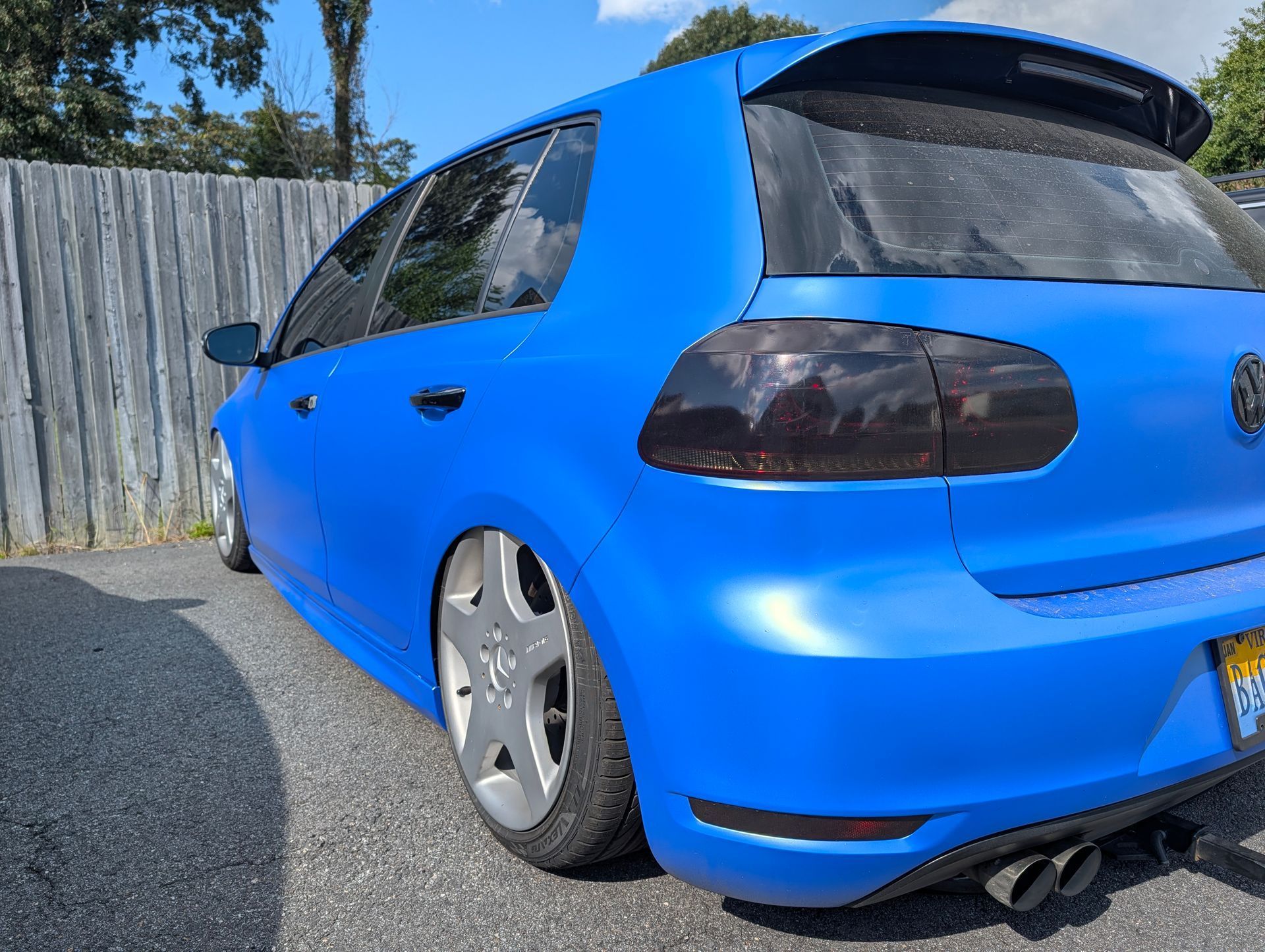 Bright blue lowered hatchback parked by a wooden fence on a sunny day