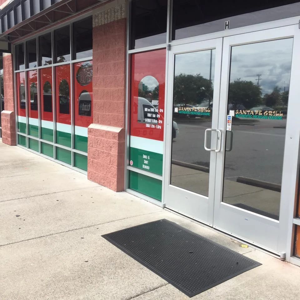 Storefront entrance with glass doors, red brick columns, and a sidewalk mat outside