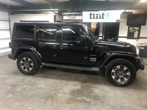 Black Jeep Wrangler parked indoors in a garage with a tint shop sign in the background