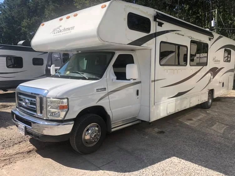 White Class C motorhome with blue stripe parked outdoors in a lot.