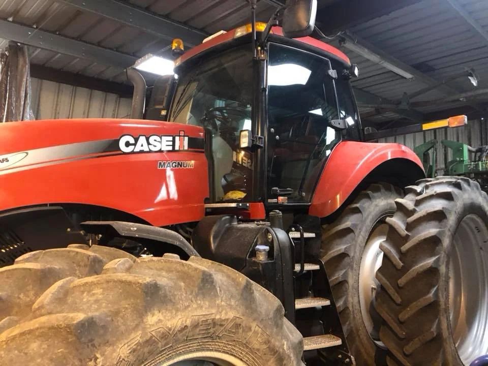 Red Case IH tractor parked inside a barn, with large muddy tires and a cab visible.