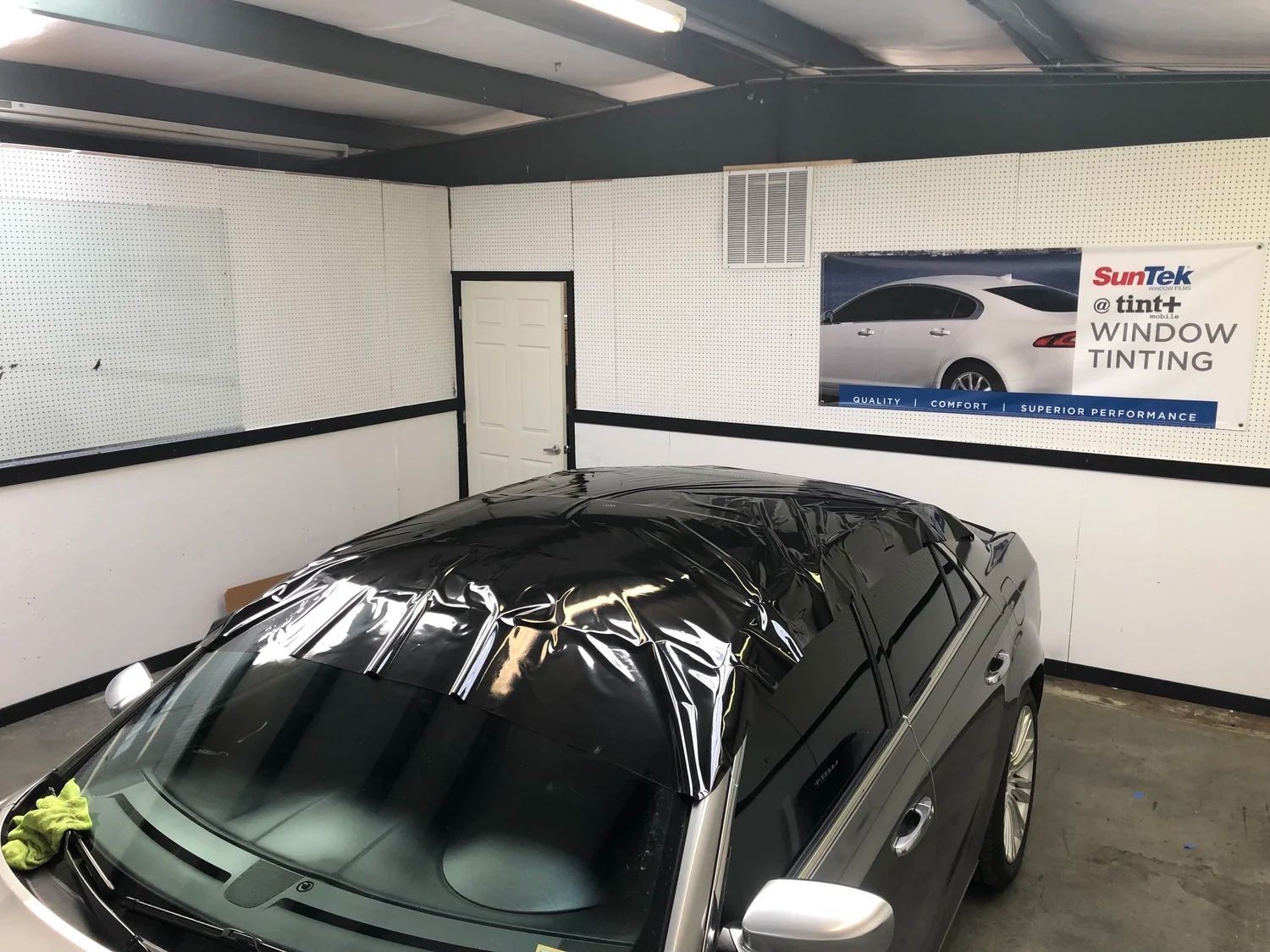Black car inside a garage with white walls and a window tinting sign on the wall