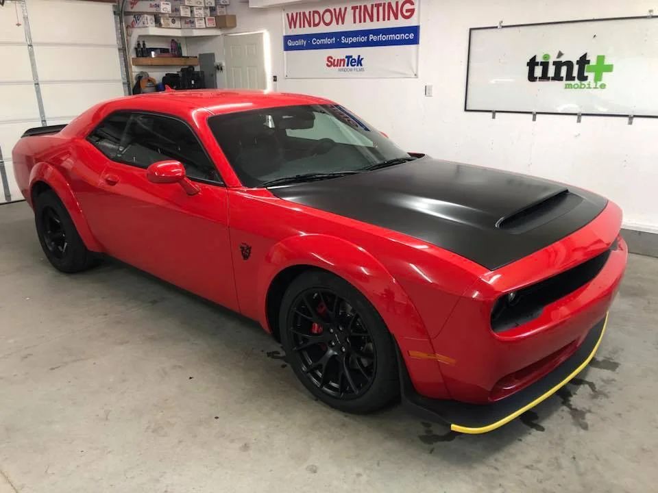 Red and black sports car in a window tint shop, with a yellow splitter guard on the front.