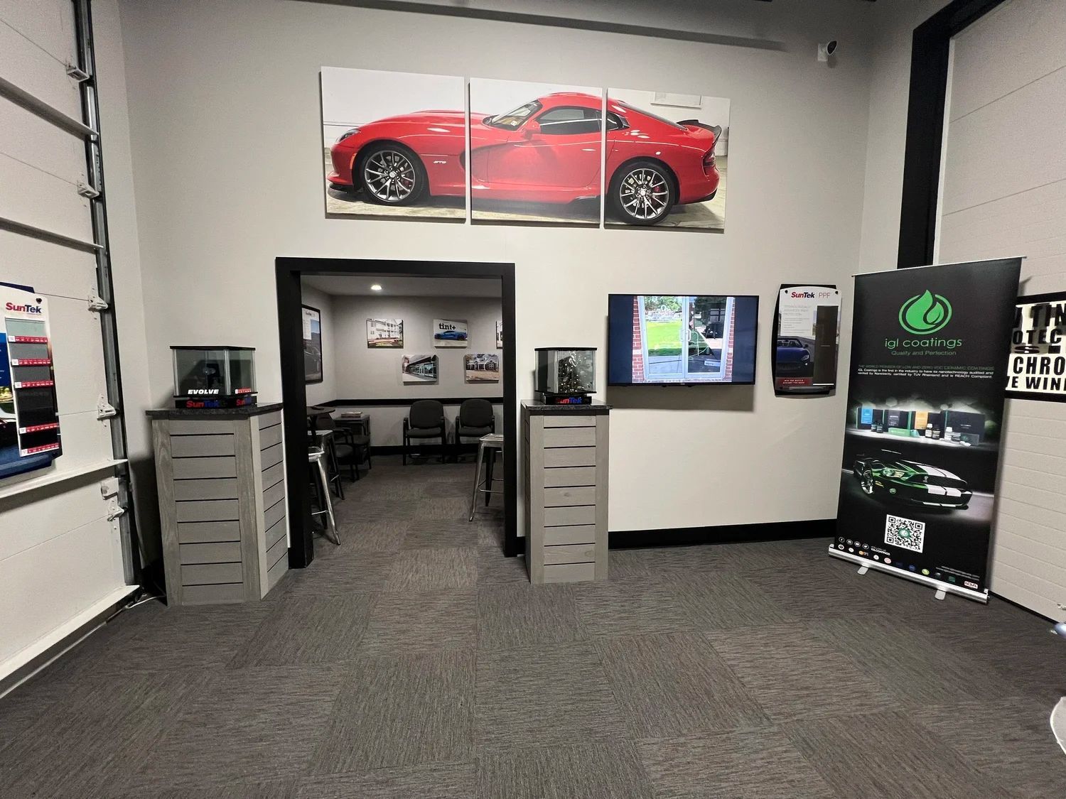 Car showroom office area with a red sports car banner, reception desks, and wall-mounted screens