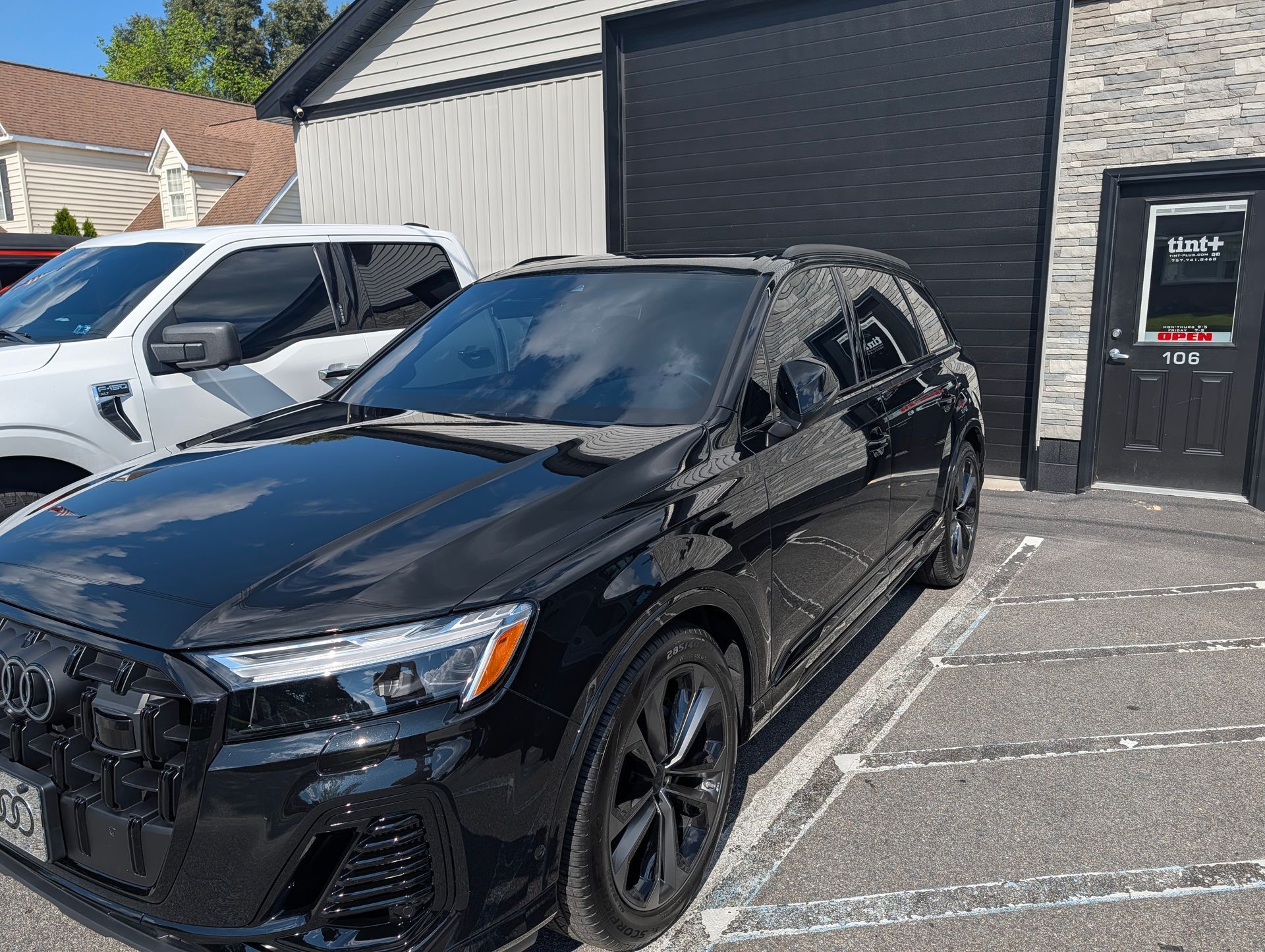 Black sedan parked outside a garage beside a white SUV on a sunny day
