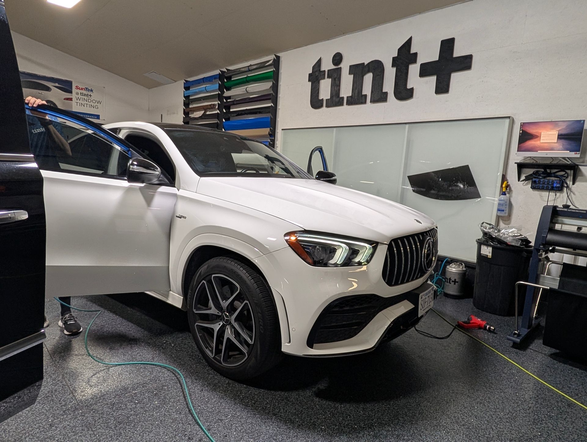 White Mercedes SUV in a car wrap shop with the door open, under the “tint+” sign.