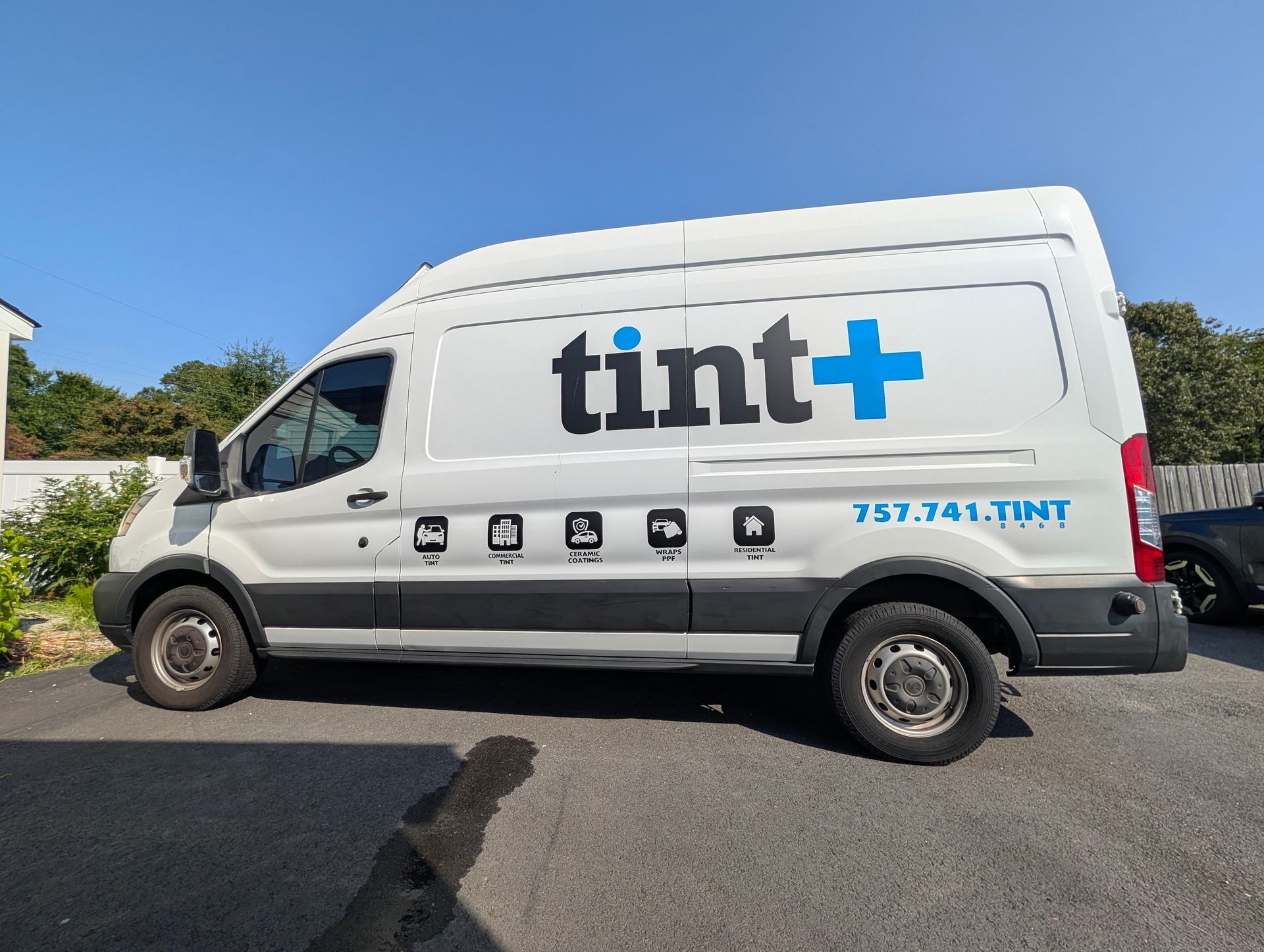 White tint+ service van parked on a street under a blue sky