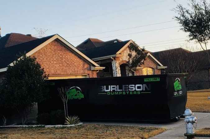 Black dumpster in front of a brick house with the logo