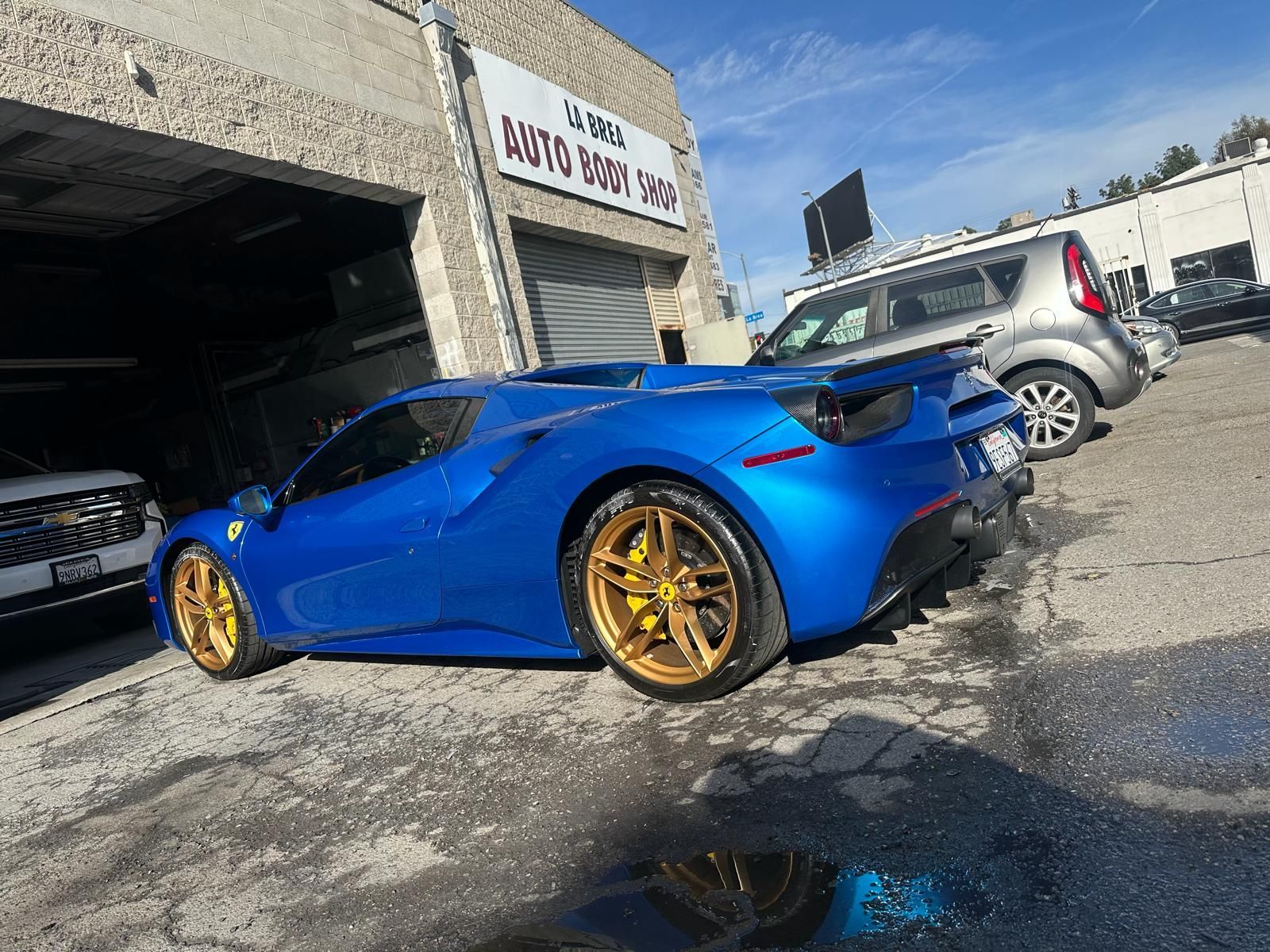 Blue sports car with gold rims parked outside a garage on a sunny day