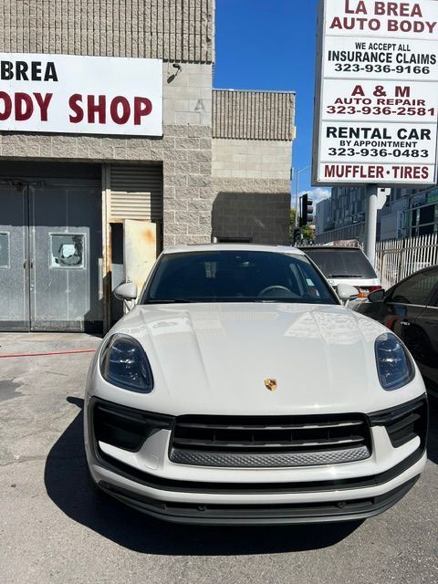 White Porsche SUV parked outside an auto body shop and rental car business.