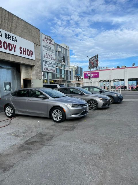 Three silver cars parked outside a body shop and storefronts under a blue sky