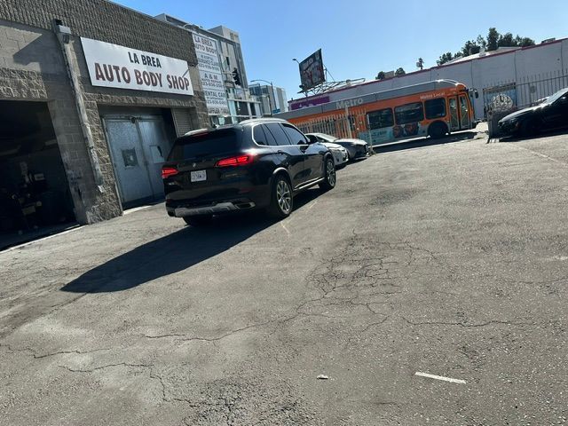 Black SUV parked outside an auto body shop on a sunny lot with a bus in the background