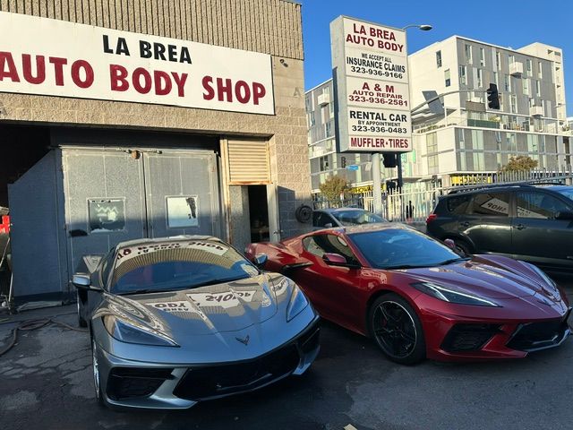 Two sports cars parked outside La Brea Auto Body Shop, one silver and one red, in daylight