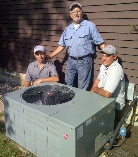 Three men are posing for a picture in front of an air conditioner