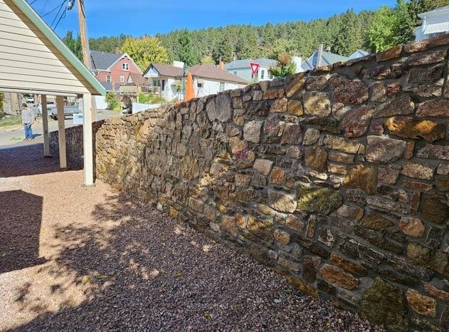 A stone wall is surrounded by gravel in front of a house.