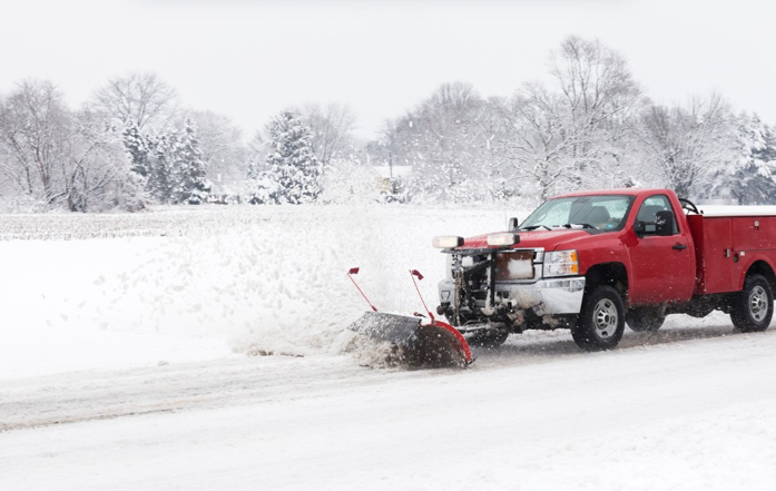 A red truck is plowing snow on a snowy road