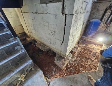 A person is standing next to a cracked wall in a basement