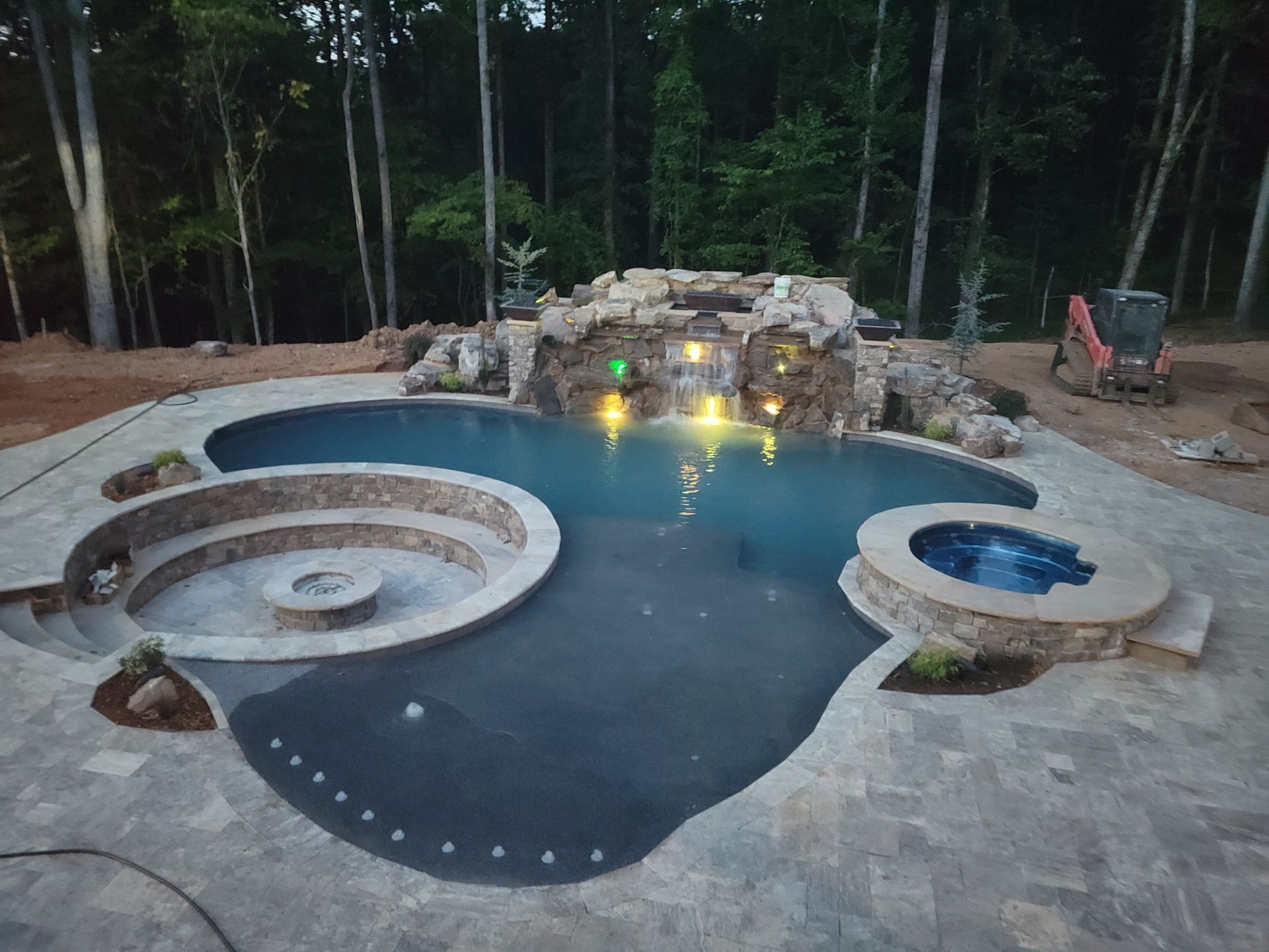 A large swimming pool with a waterfall and a fire pit