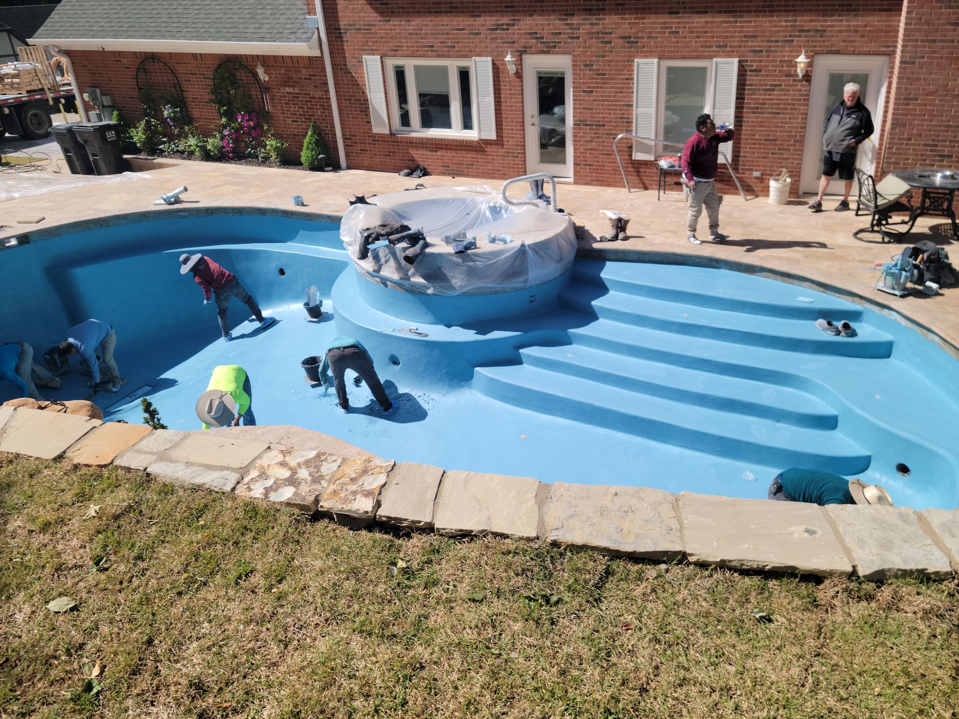 A group of people are working on a swimming pool in front of a brick house.